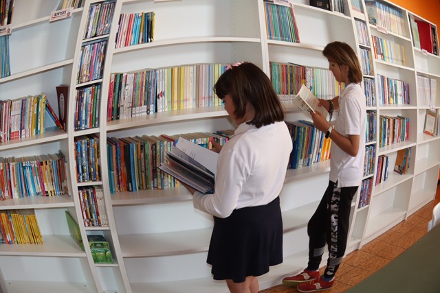 Studentesse del Collegio scelgono libri dagli scaffali della biblioteca scolastica